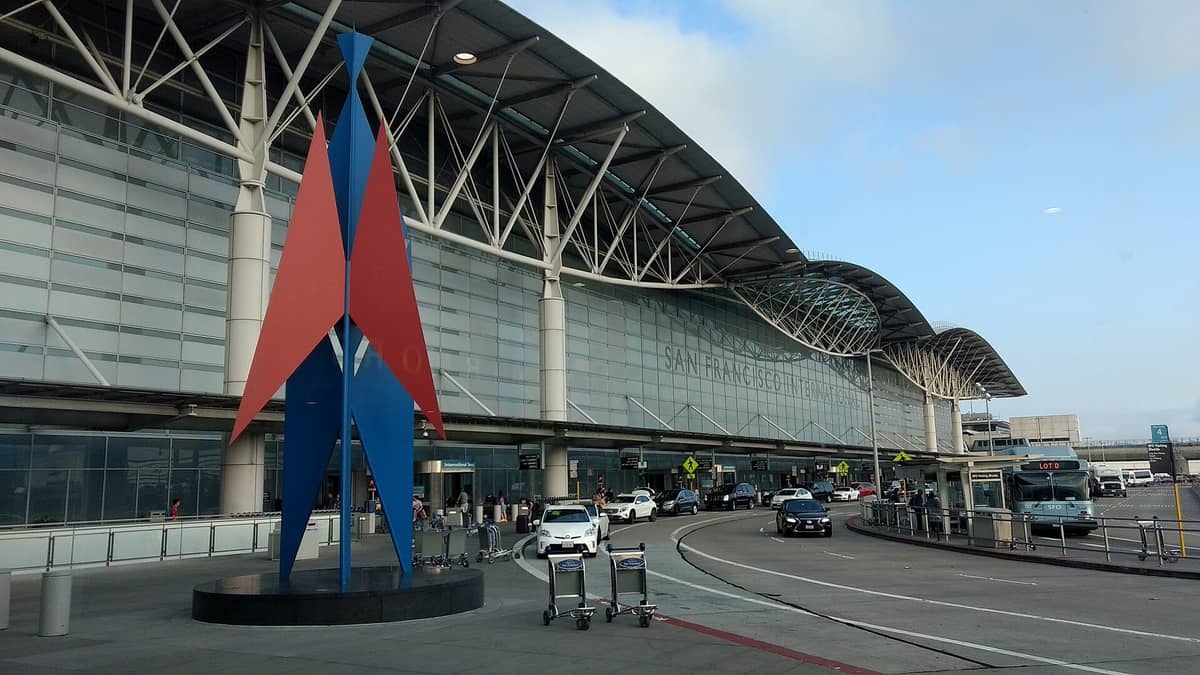 Außenansicht vom Bordstein des Hauptterminals des San Francisco International Airport mit einem Schild mit der Aufschrift San Francisco International, Autos, Bussen und einer modernen Glasfassade.