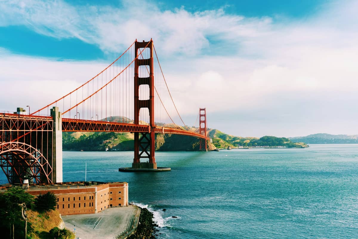 Die Golden Gate Bridge überspannt die Bucht mit Fort Point darunter, blauer Himmel und Wasser — das Wahrzeichen San Franciscos an einem klaren Tag.