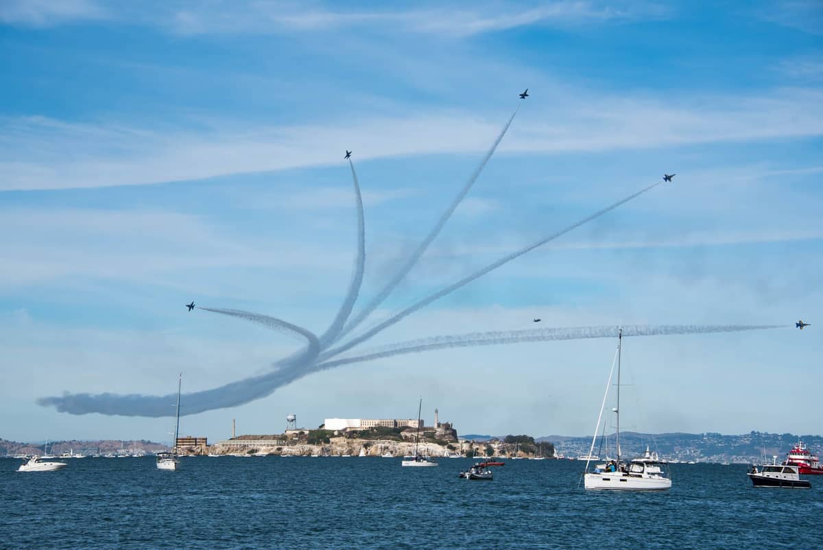 Jets del espectáculo aéreo actuando sobre la Bahía de San Francisco con Alcatraz Island, barcos y espectadores visibles en primer plano.