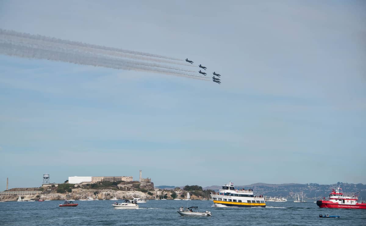 El equipo de vuelo Blue Angels realizando un show aéreo sobre la Bahía de San Francisco, con botes en el agua y la isla de Alcatraz visible al fondo.