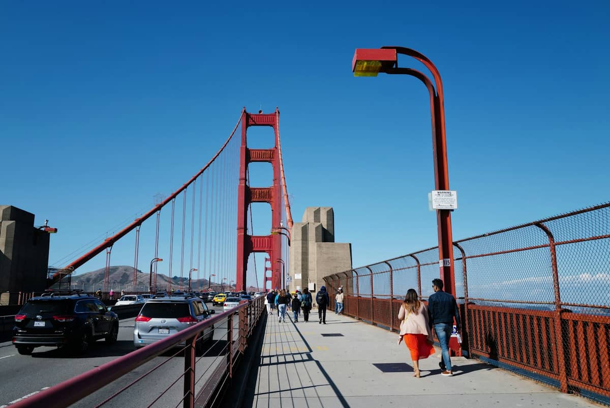 Menschen, die gemeinsam auf dem Fußgängerweg der Golden Gate Bridge unter einem klaren blauen Himmel spazieren.