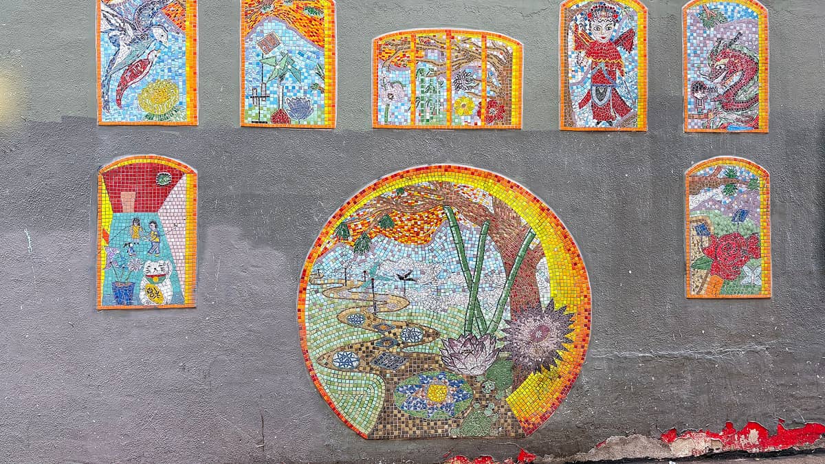 Coloridos murales de mosaico de azulejos en una pared gris en el Chinatown de San Francisco, con arte local y escenas culturales que representan las joyas del arte callejero.