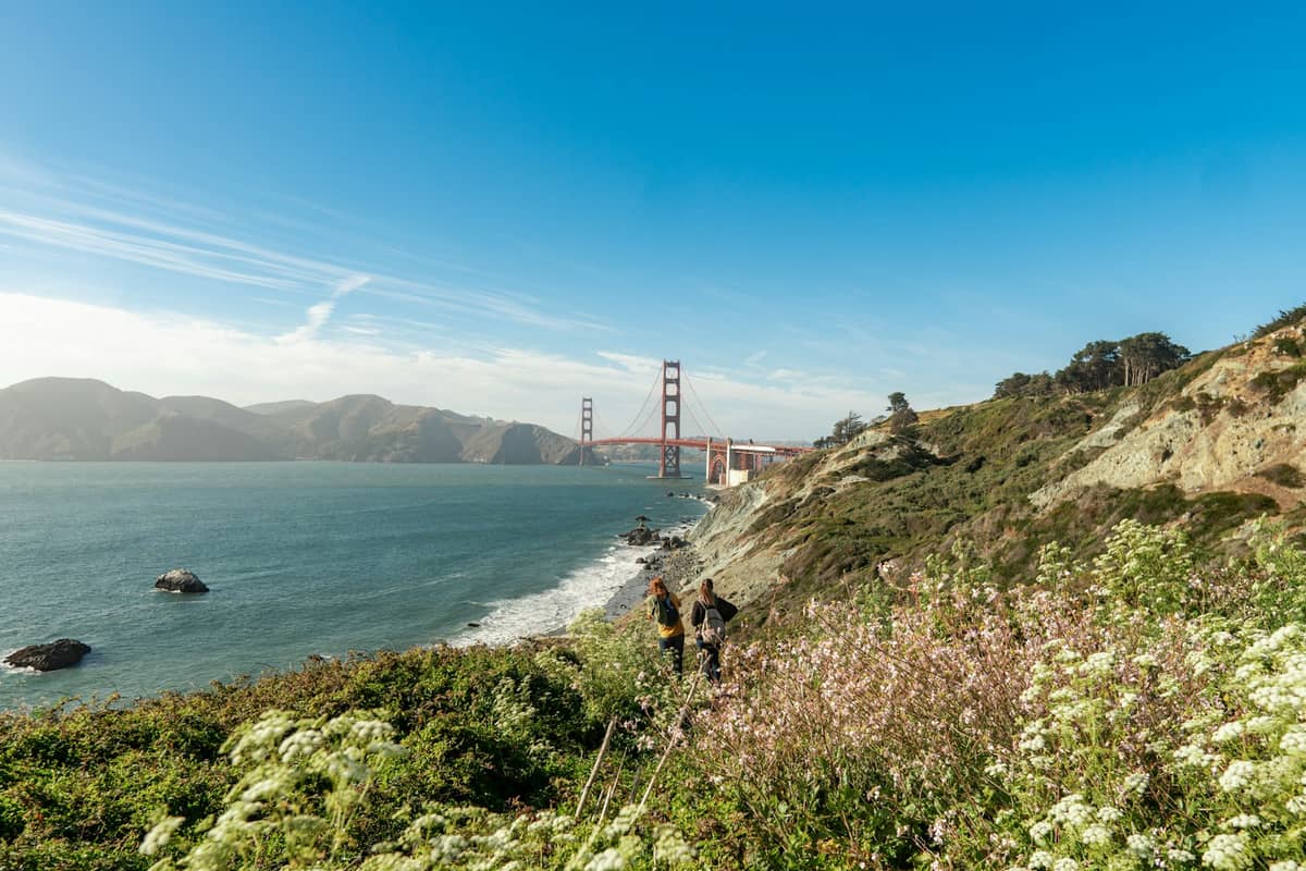 Excursionistas caminan por el Sendero Costero de California sobre los acantilados del océano con el puente Golden Gate al fondo en un día despejado en San Francisco.