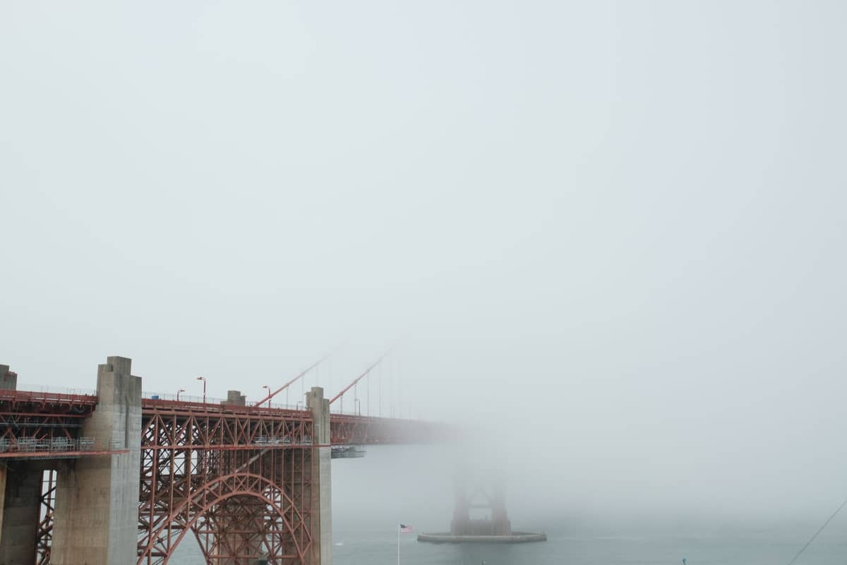 Golden Gate Bridge oculto por una densa niebla veraniega, con solo parte de su estructura visible contra un cielo gris.