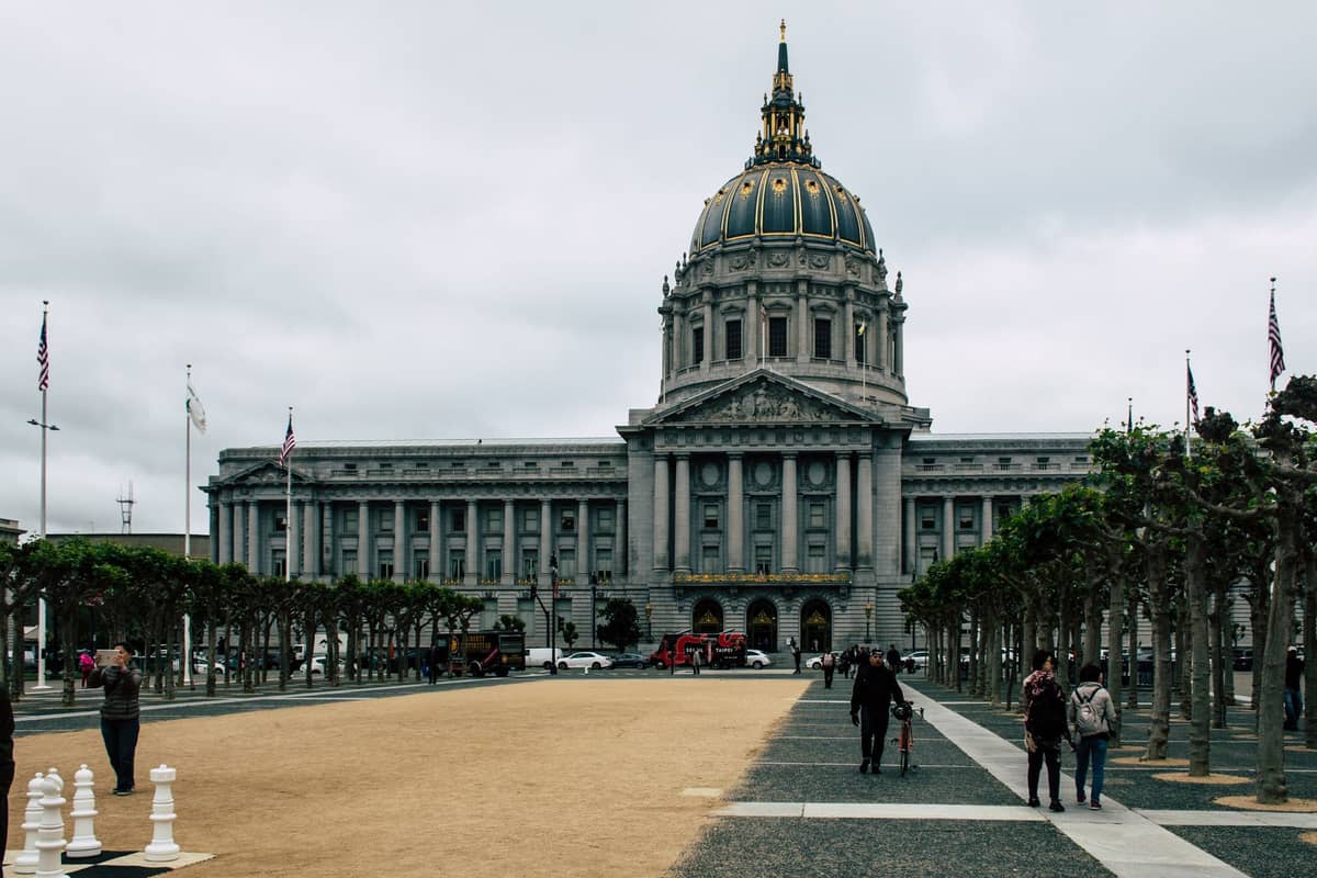 El Ayuntamiento de San Francisco con personas caminando y grandes piezas de ajedrez afuera, capturando el área del Civic Center durante el día.