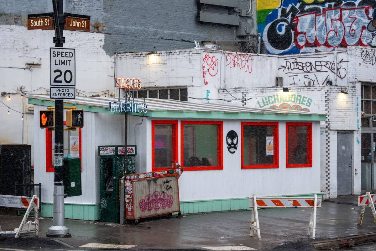Mała taqueria z neonowym szyldem tacos i burritos na pokrytym graffiti rogu Mission District nocą.