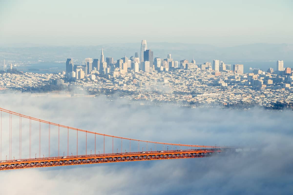 Golden Gate Bridge spowity mgłą z panoramą San Francisco widoczną w tle pod bezchmurnym niebem