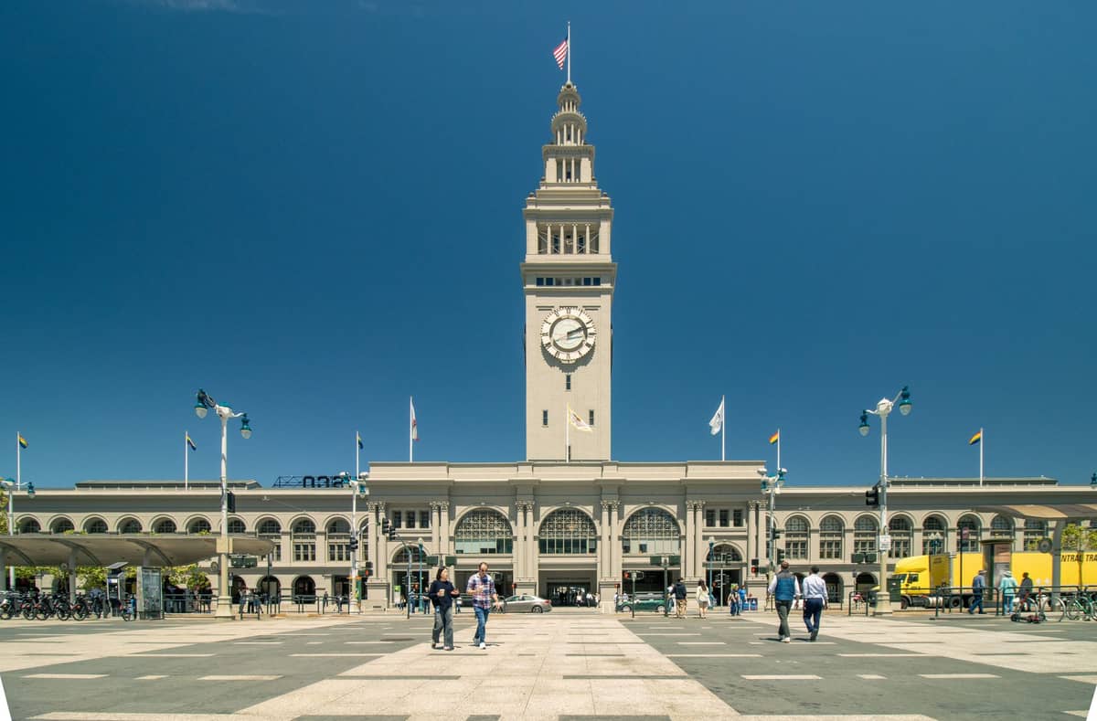 วิวกลางวันของ San Francisco Ferry Building พร้อมหอนาฬิกา ท้องฟ้าแจ่มใส และผู้คนเดินอยู่เบื้องหน้า