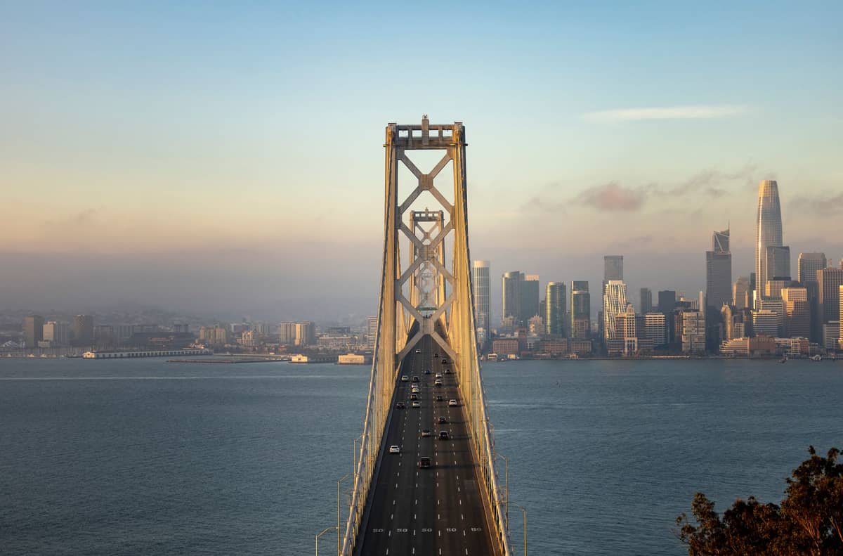 สะพาน San Francisco Bay Bridge มุ่งสู่ใจกลางเมืองโดยมีเส้นขอบฟ้าของเมืองปรากฏให้เห็นในพื้นหลังช่วงพลบค่ำ