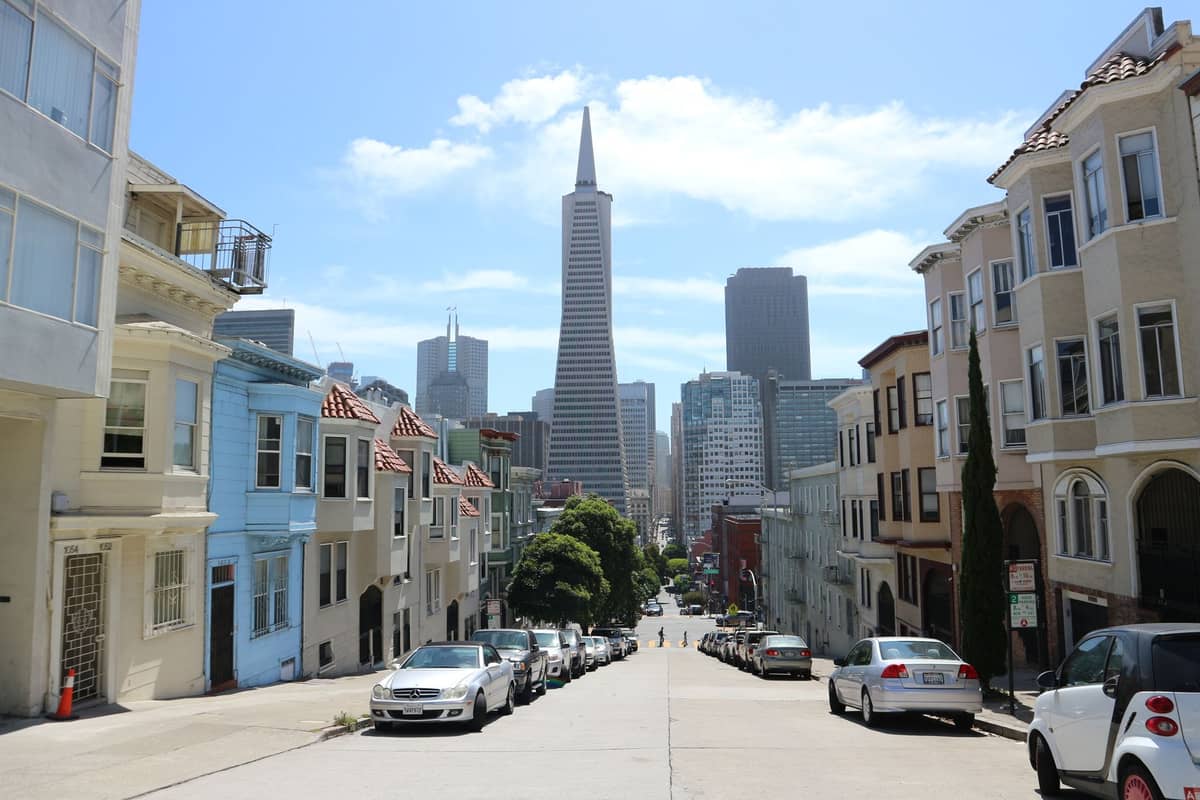 วิวถนนในซานฟรานซิสโกพร้อม Transamerica Pyramid ท้องฟ้าสีฟ้า และอากาศฤดูใบไม้ผลิที่แสนสดใส เห็นแถวบ้านและรถยนต์จอดเรียงราย