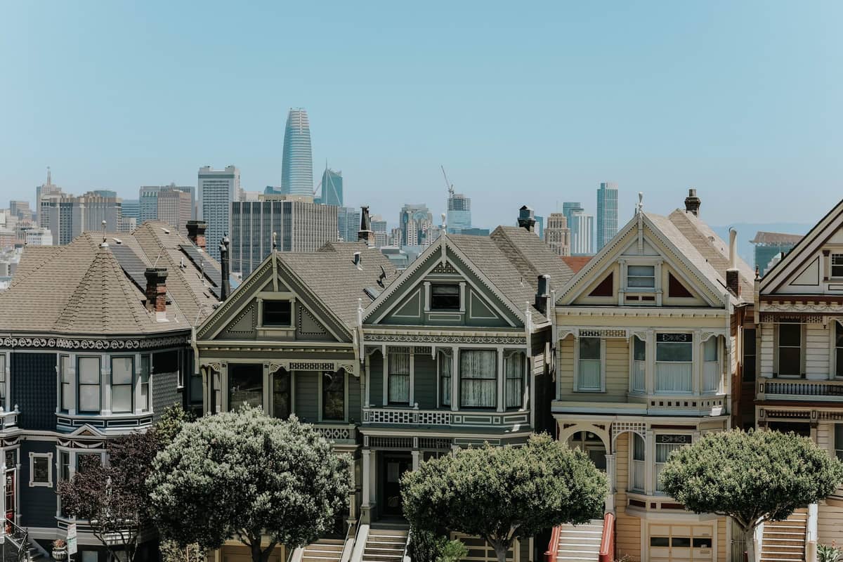 Reihe ikonischer viktorianischer Häuser mit der Skyline der Innenstadt von San Francisco im Hintergrund an einem klaren Tag