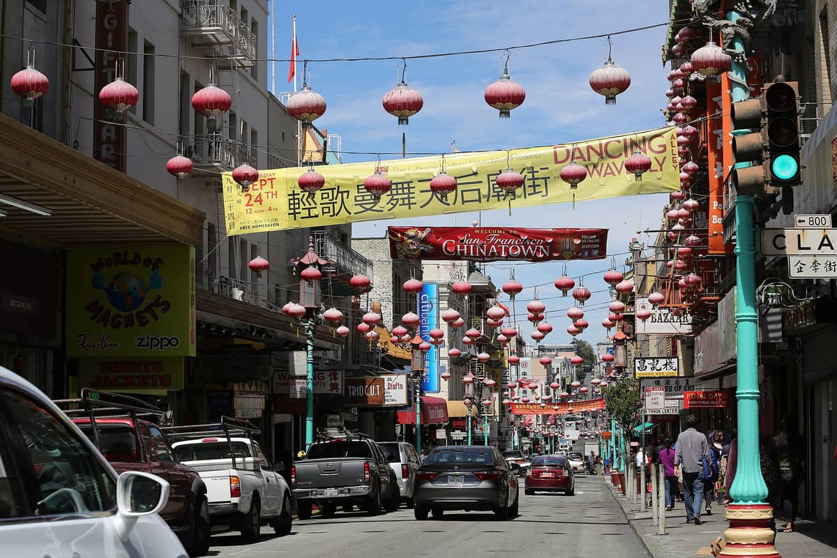 Straßenansicht von San Francisco Chinatown mit hängenden roten Laternen, Bannern, Geschäften und Menschen, die die belebte Straße entlanggehen.
