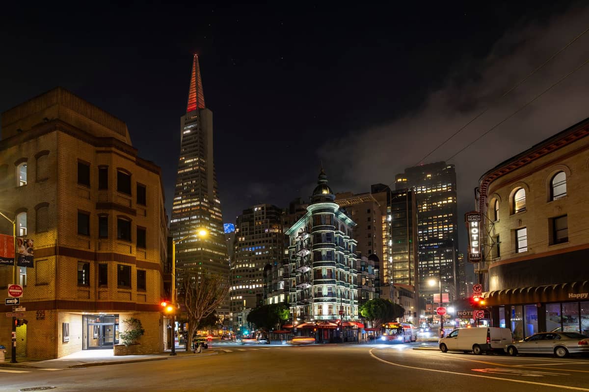 Pemandangan jalan malam di San Francisco dengan Transamerica Pyramid dan Columbus Tower, menonjolkan kehidupan malam kota yang semarak di dekat area klub populer.