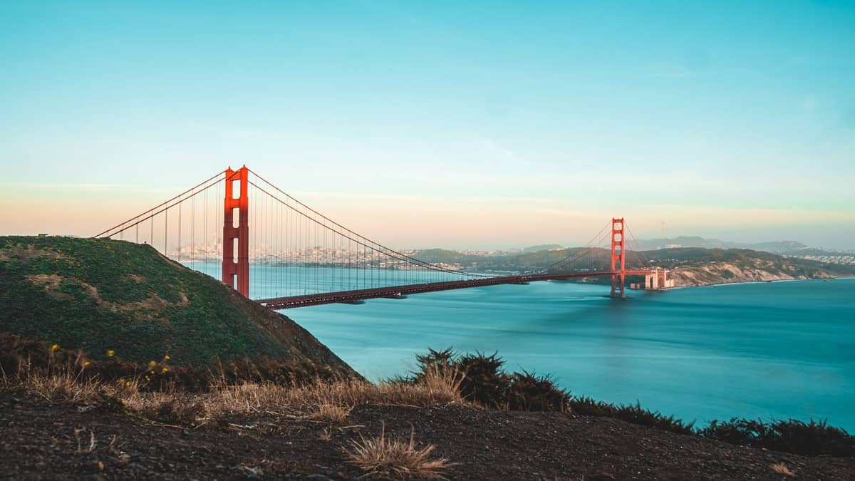 Vista panorámica del Golden Gate Bridge en San Francisco al amanecer, con aguas azules y colinas verdes al fondo.