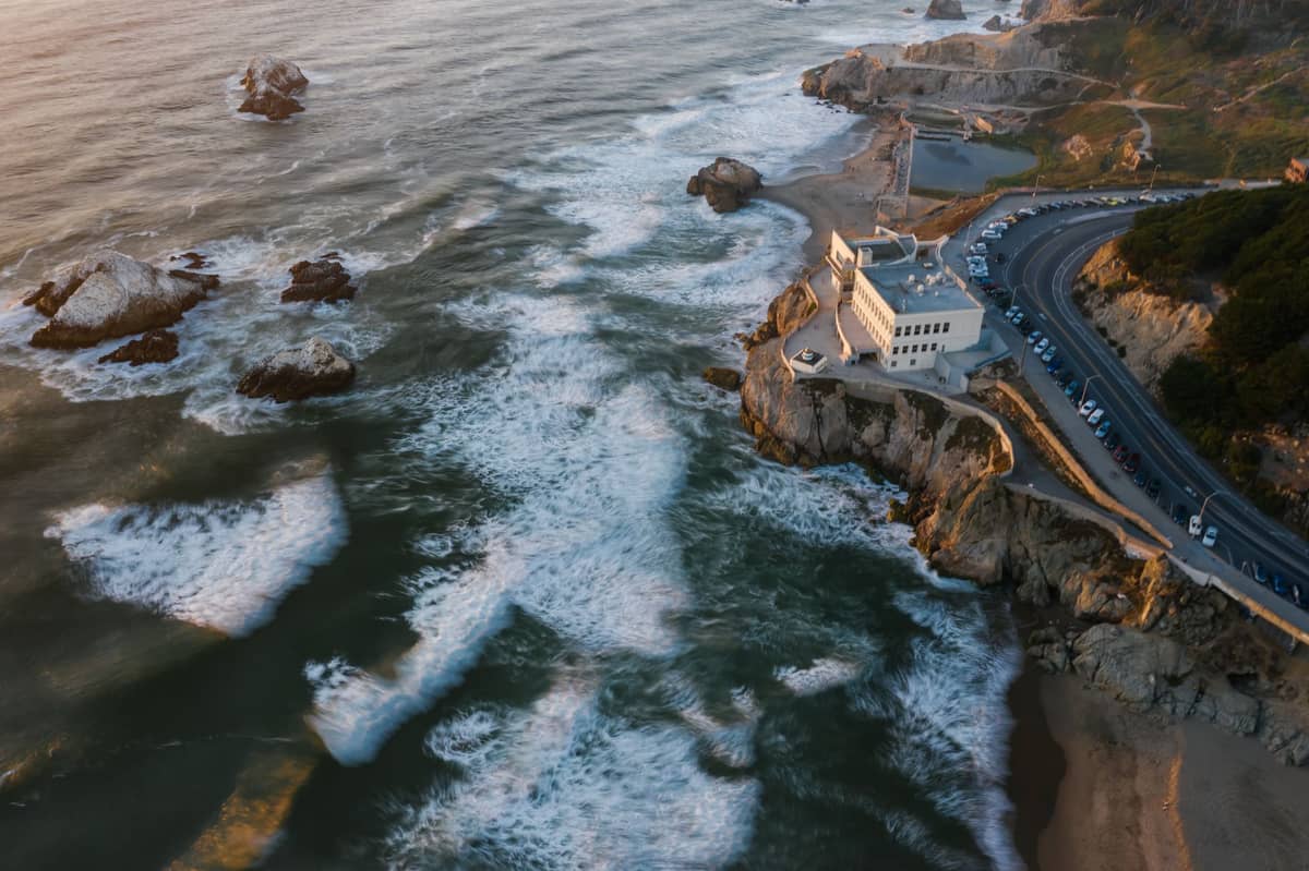 Luftaufnahme der Ruinen der Sutro Baths und des Cliff House in San Francisco bei Sonnenuntergang mit Wellen, die an der felsigen Pazifikküste brechen.