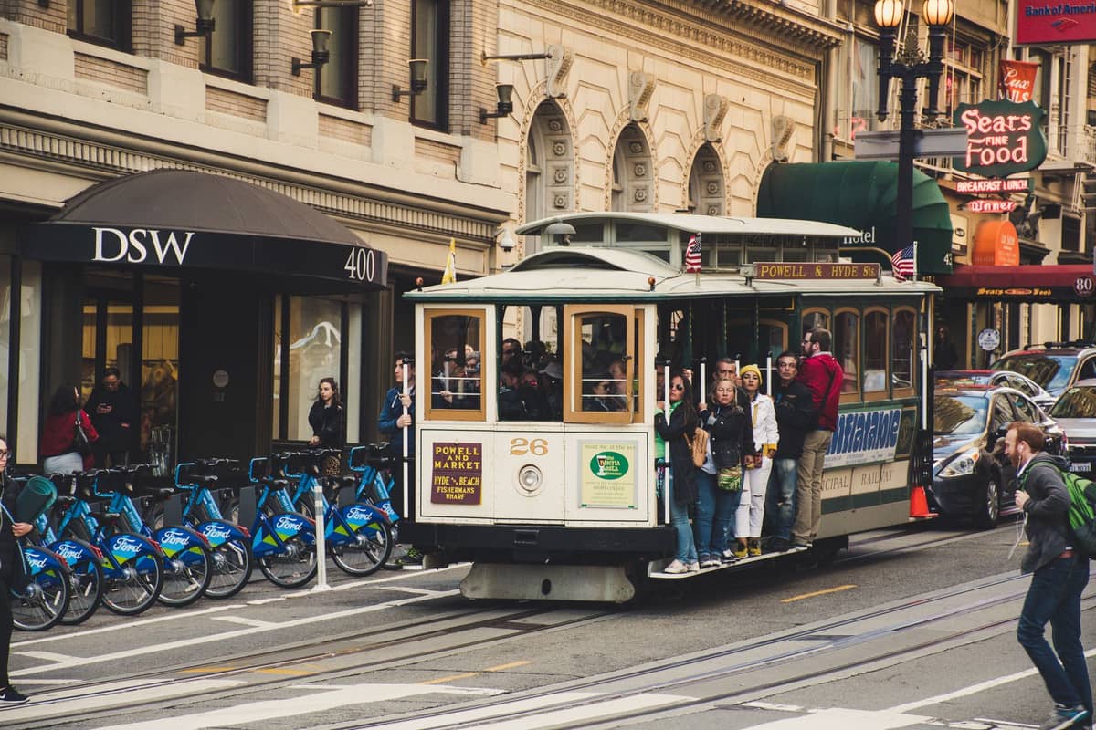 Kolejka linowa w San Francisco z wieloma turystami stojącymi i jadącymi w pobliżu ruchliwych sklepów przy Union Square w ciągu dnia.