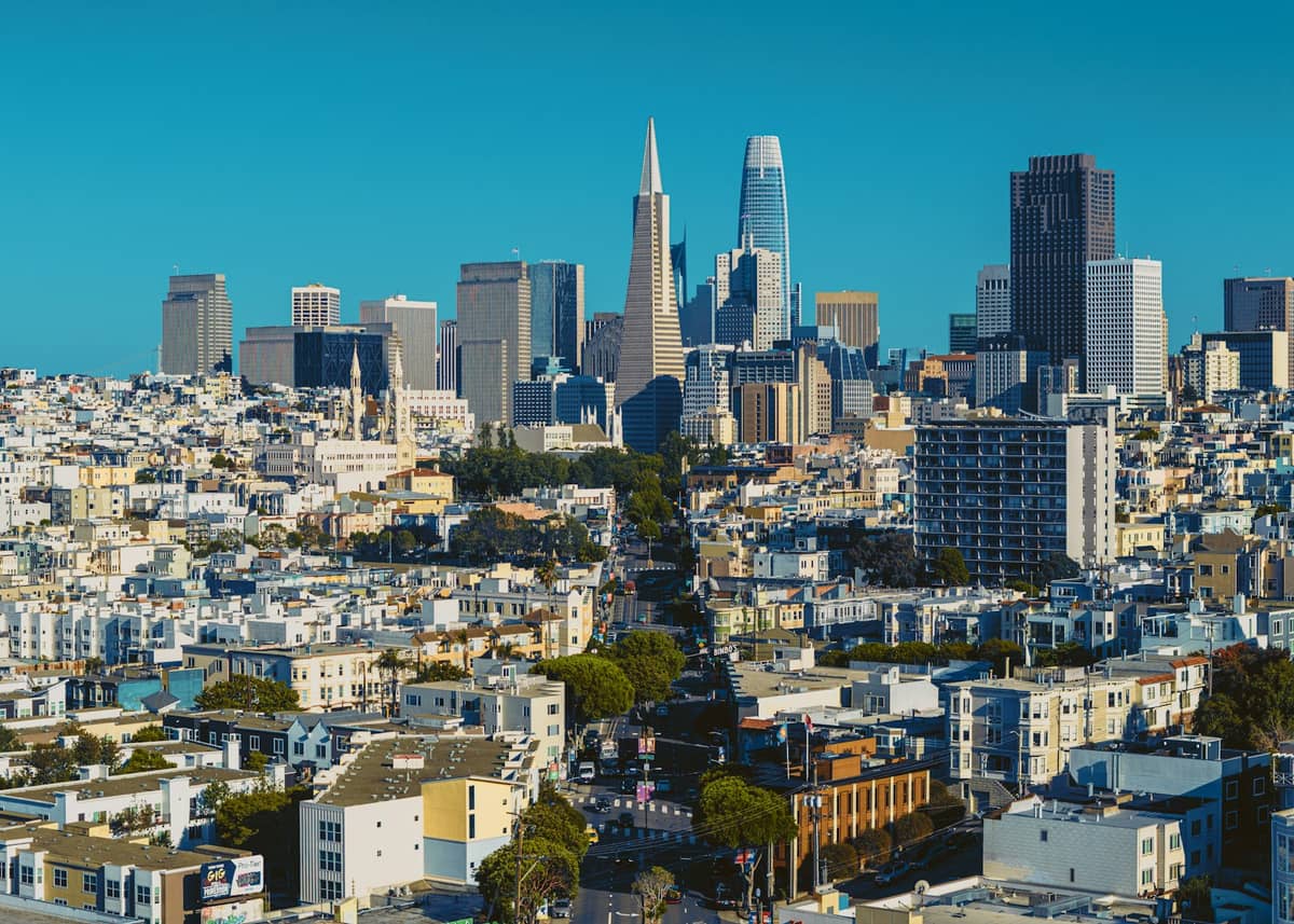 San Francisco skyline featuring iconic Transamerica Pyramid and Salesforce Tower with clear blue sky and densely packed buildings in the foreground.