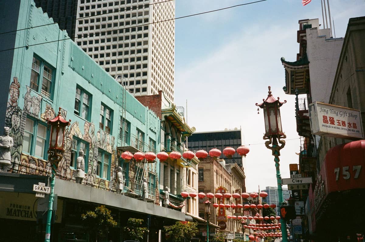 Vista della strada del Chinatown di San Francisco con il cartello di Grant Avenue, lanterne colorate, facciate di edifici ornate e un grattacielo sullo sfondo.