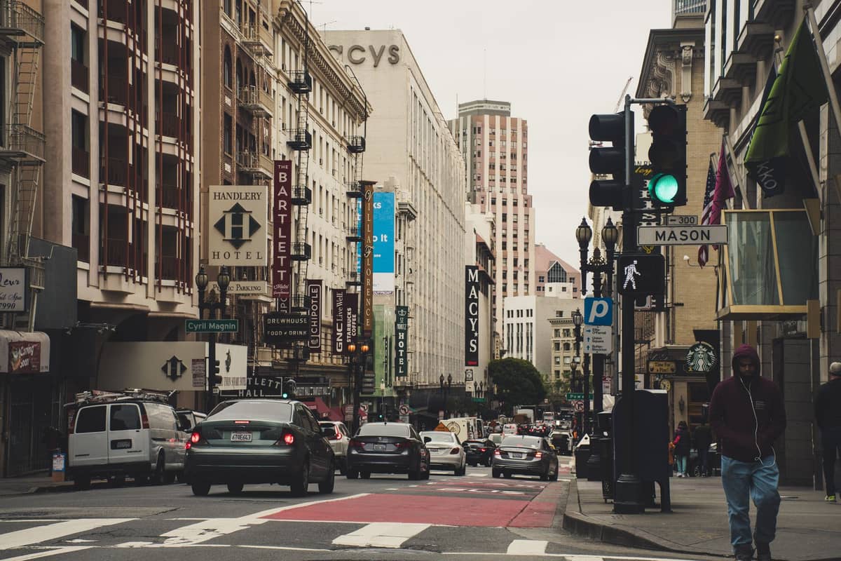 Vista de la zona comercial de Union Square en San Francisco con Macy's y otras grandes tiendas, carteles de comercios, peatones y edificios del centro.