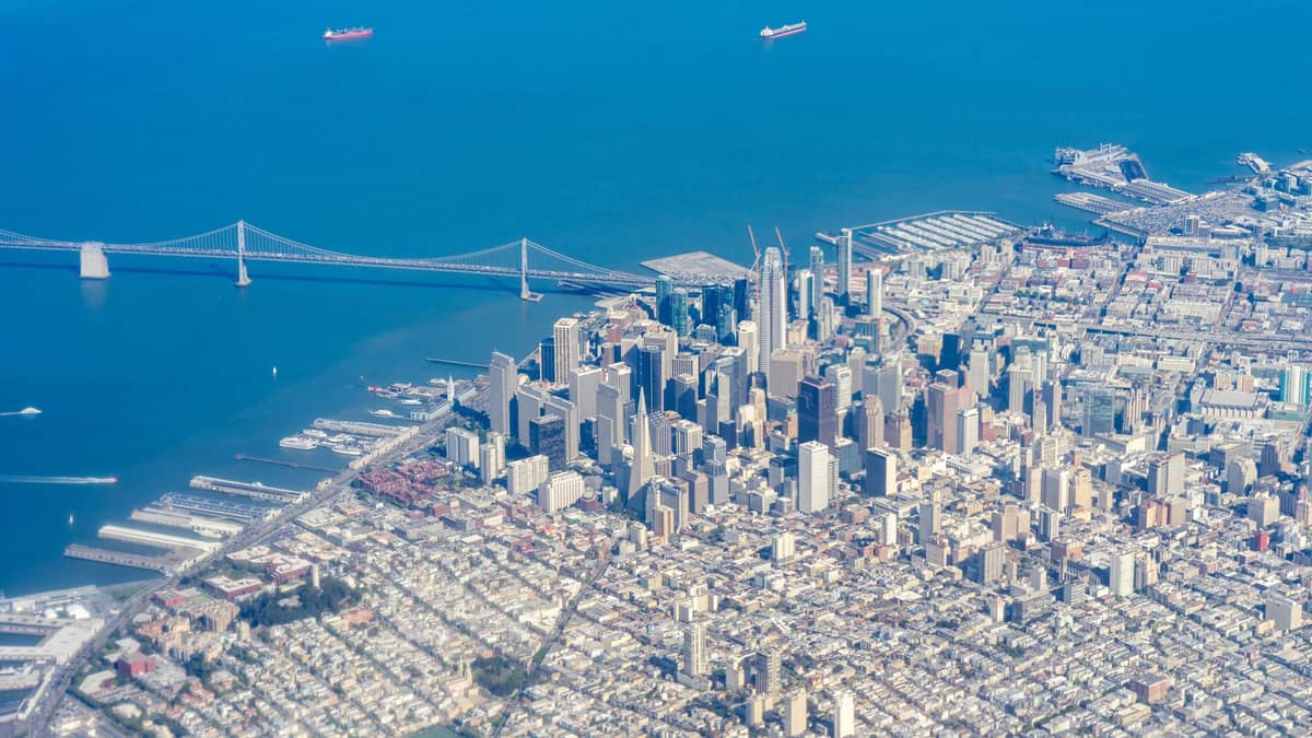 Luftaufnahme der Innenstadt von San Francisco und der Bay Bridge mit Stadtstraßen, Wasser und Schiffen in der Bucht.