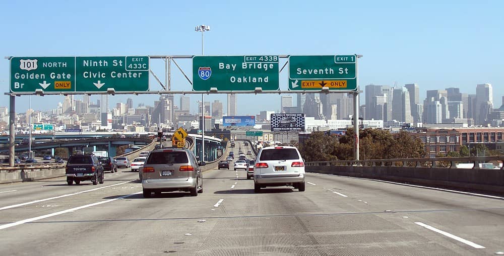 Blick von einer Autobahn in Richtung San Francisco, mit deutlichen Straßenschildern für US 101 North, I-80 und Downtown, und der Skyline der Stadt voraus.