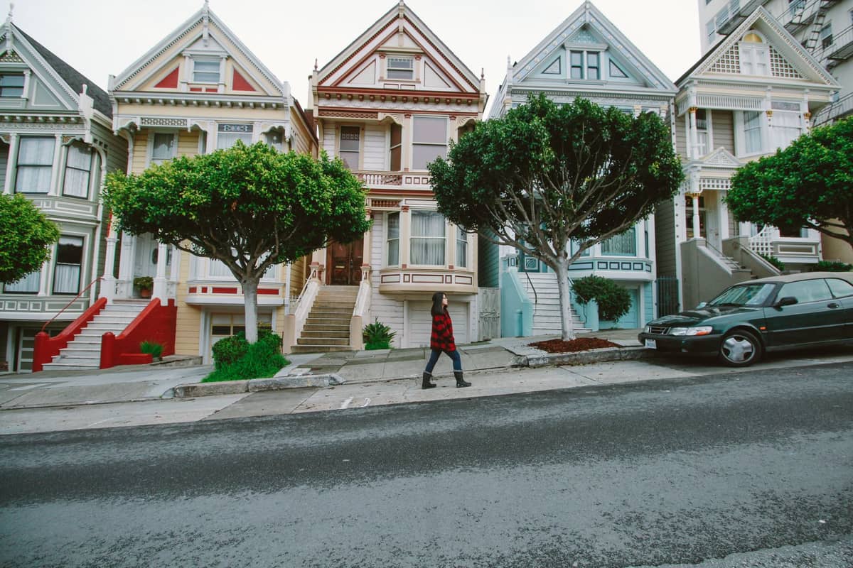 Una persona caminando frente a las famosas Painted Ladies de San Francisco, una hilera de coloridas casas victorianas con árboles y una calle en pendiente.