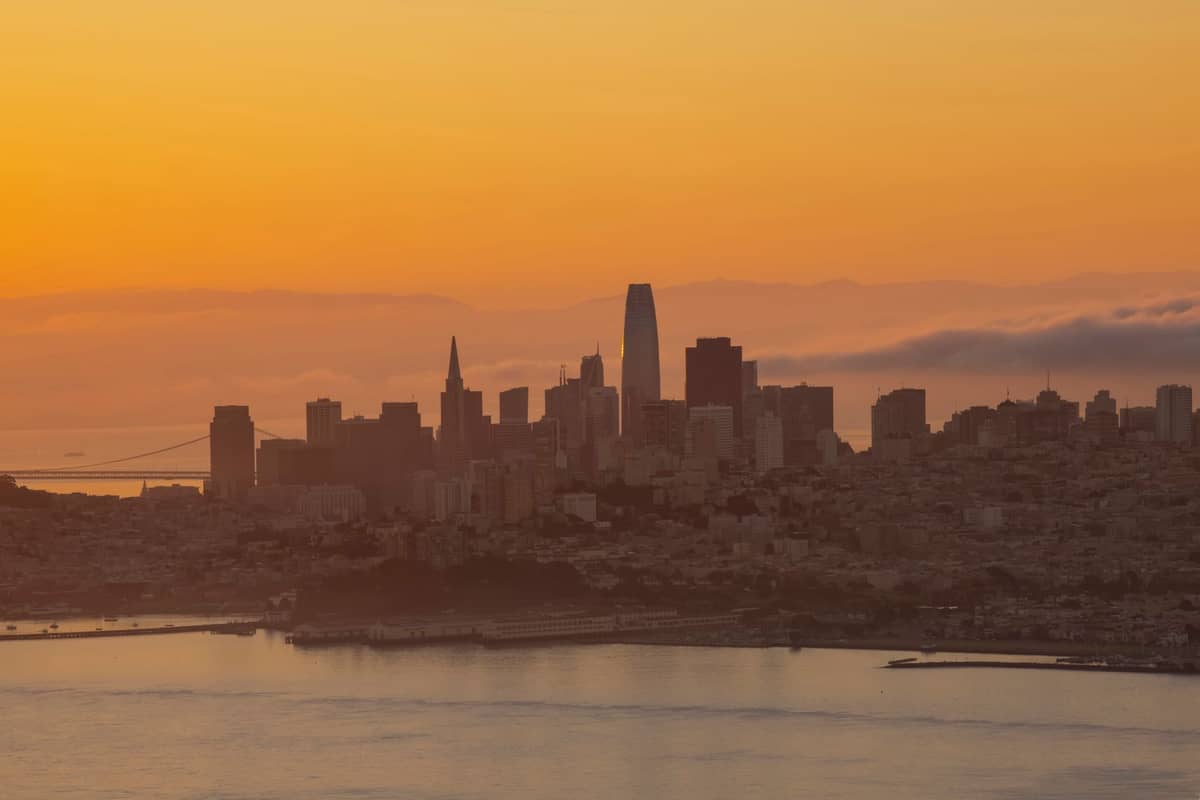 El horizonte de San Francisco al atardecer con la Torre Salesforce, la Pirámide Transamerica y los edificios de la ciudad vistos desde la bahía bajo un cielo anaranjado.
