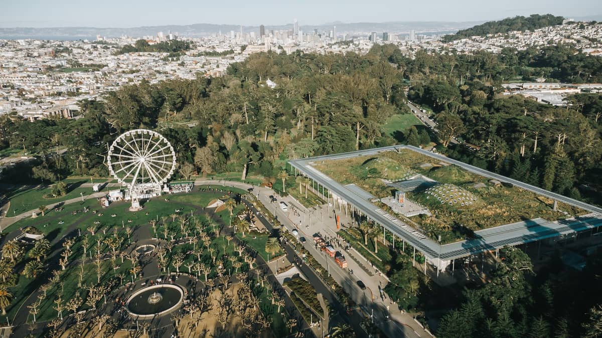 Luftaufnahme des Golden Gate Park in San Francisco mit der California Academy of Sciences und ihrem begrünten Dach, einem Riesenrad und der Skyline der Stadt.