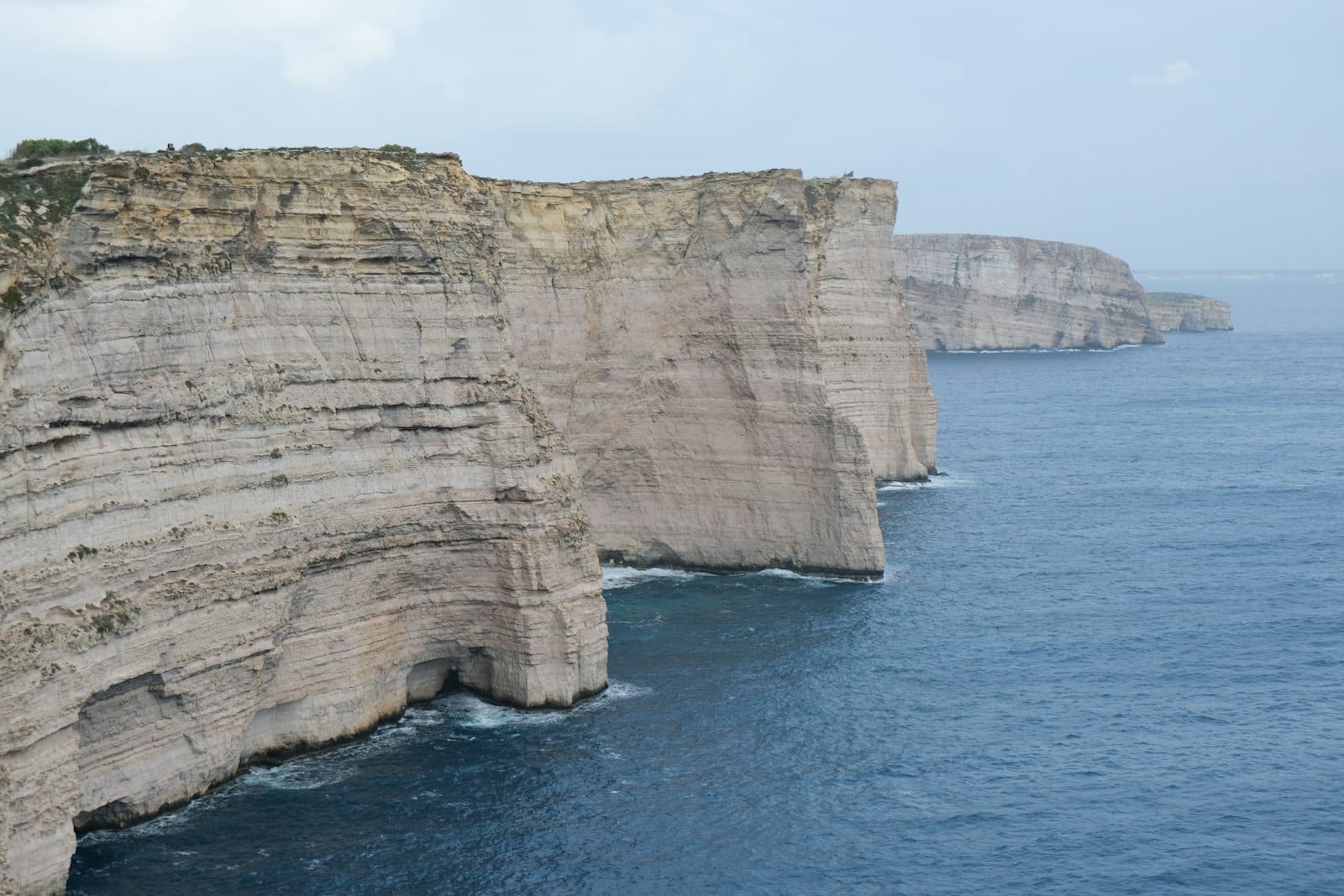Le ripide scogliere calcaree di Sanap Cliffs si innalzano spettacolarmente sul profondo Mar Mediterraneo blu lungo la costa meridionale incontaminata di Gozo, sotto un cielo leggermente nuvoloso.