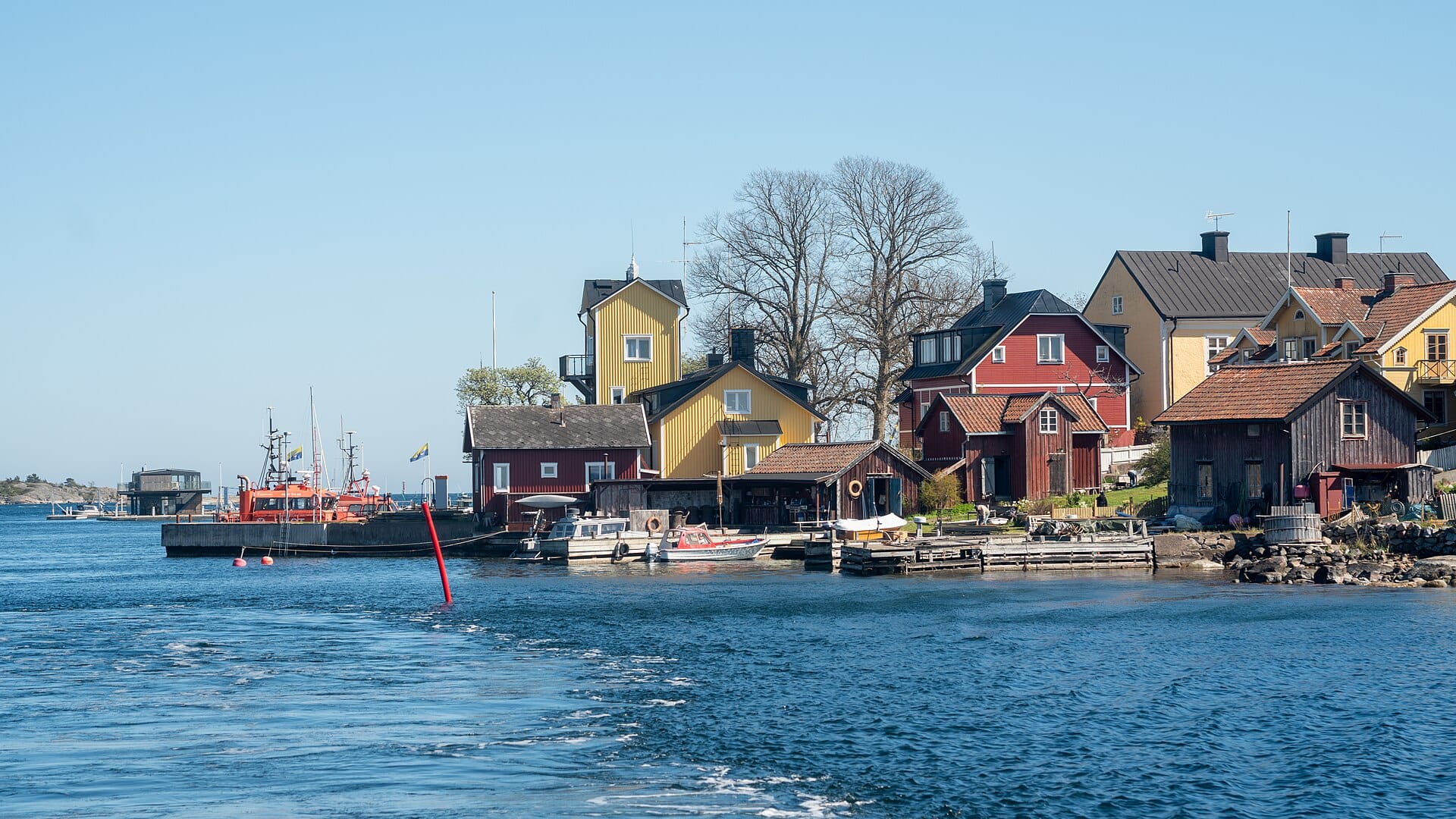 วิวท่าเรือ Sandhamn กับบ้านไม้สีสันสดใส เรือจอดเรียงราย น้ำทะเลสีฟ้าใสและฟ้าสดใสในหมู่เกาะสต็อกโฮล์ม