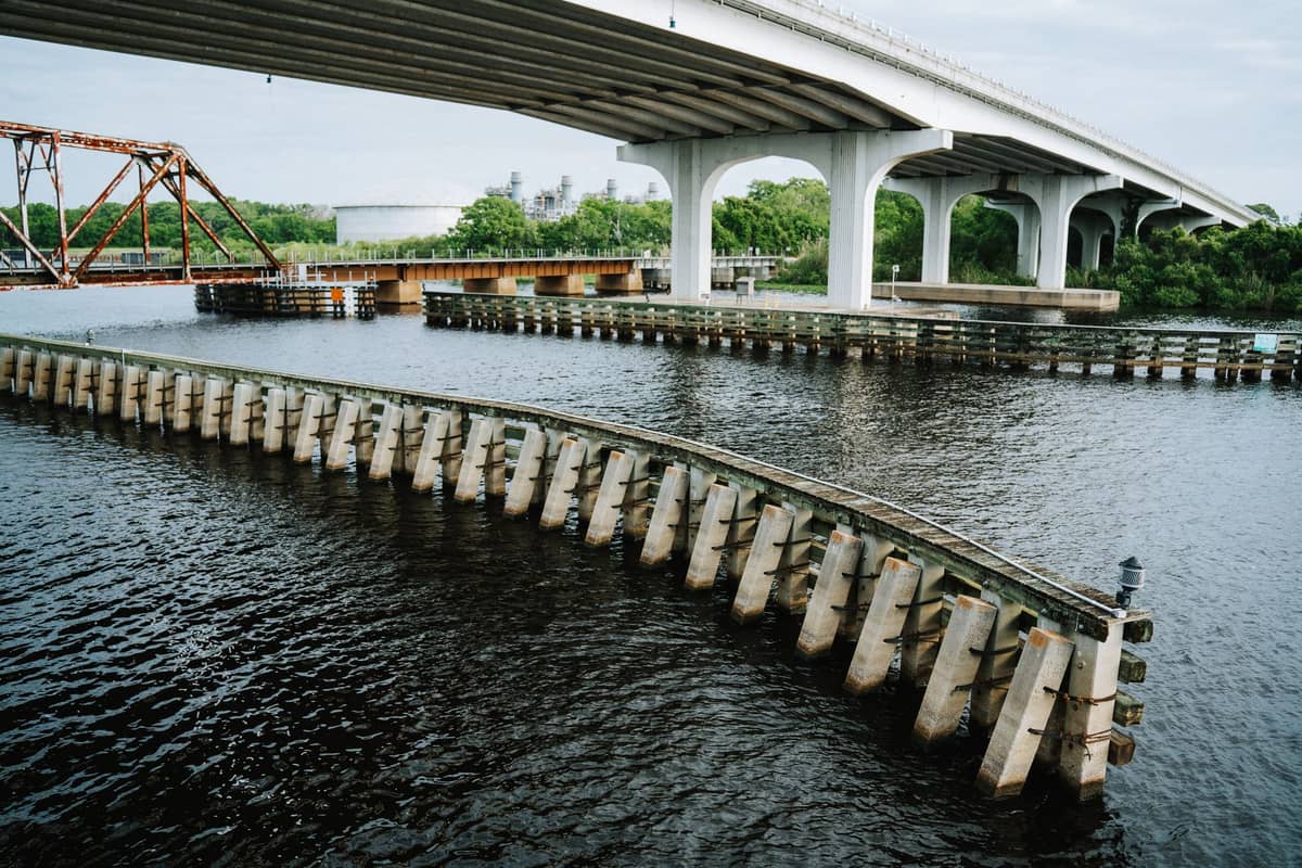 Weitwinkelpanorama des Sanford RiverWalk mit Marina, Fußweg und zwei parallelen Brücken, die den Lake Monroe unter bewölktem Himmel überqueren.
