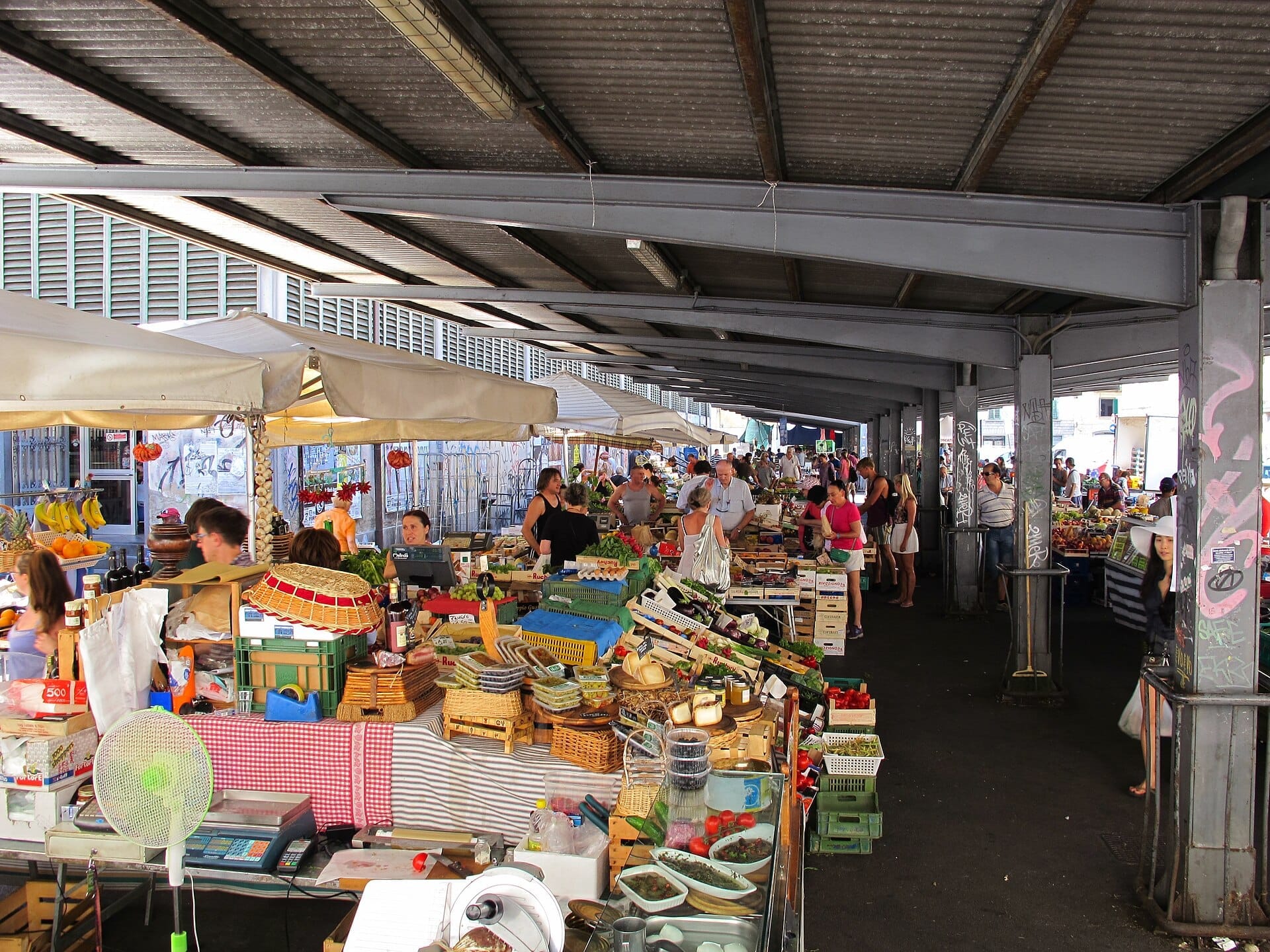 ผู้ขายและนักช้อปรวมตัวกันใต้หลังคาของตลาด Sant'Ambrogio ในเมืองฟลอเรนซ์ ท่ามกลางสินค้าสีสันสดใสและแผงขายของในตลาด