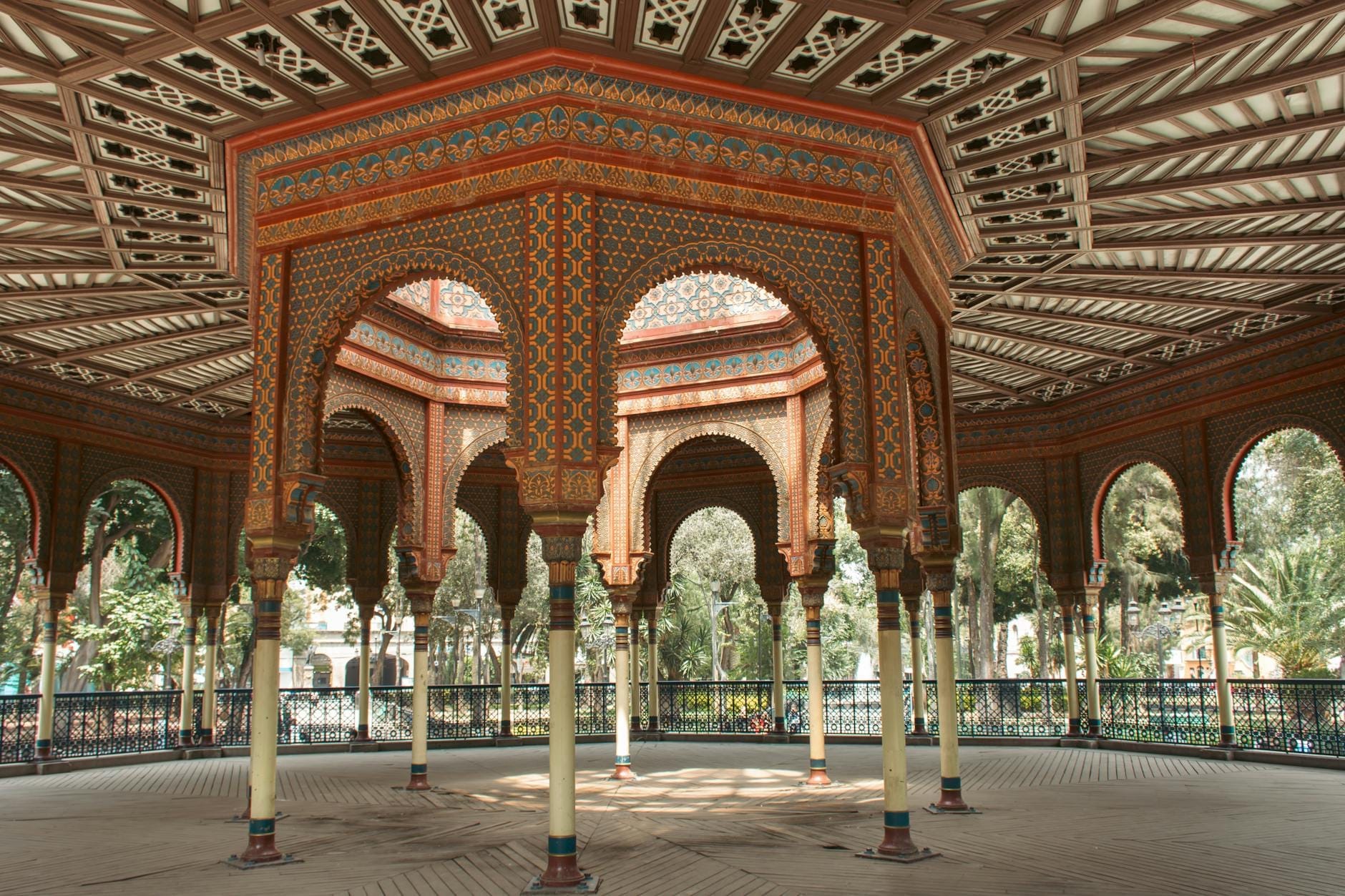 Vista interna del Kiosco Morisco di Città del Messico con archi moreschi ornati, struttura ottagonale, motivi decorativi intricati e luce naturale che filtra in un contesto di parco alberato.