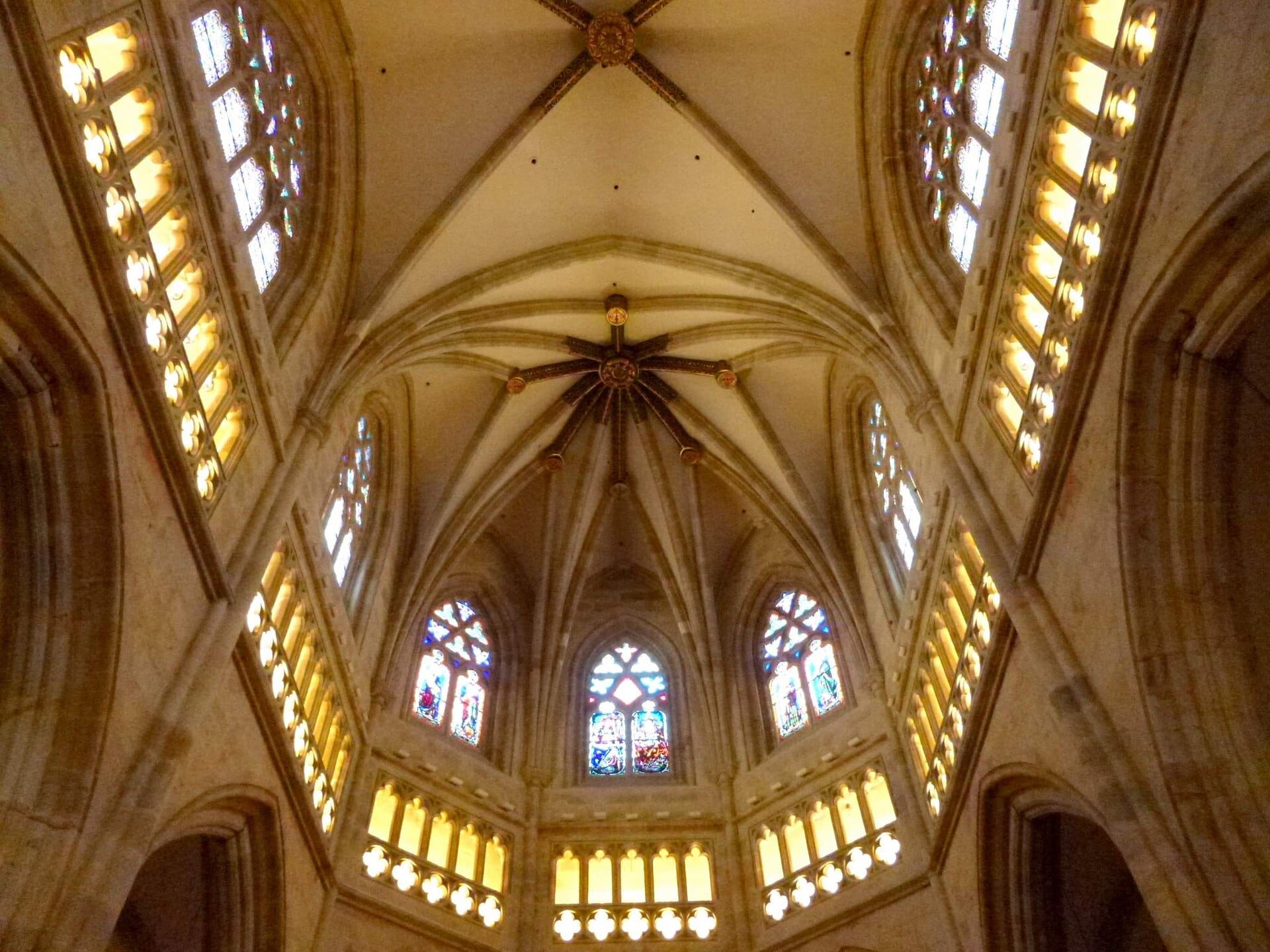Interior view of Santiago Cathedral in Bilbao, showcasing the intricate Gothic ribbed vaults and stained glass windows bathed in warm golden light.