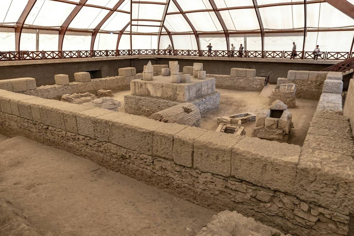 Innenansicht der großen archäologischen Stätte Akrotiri auf Santorini mit antiken Steinruinen und teilweise rekonstruierten Mauern unter einem Schutzdach.