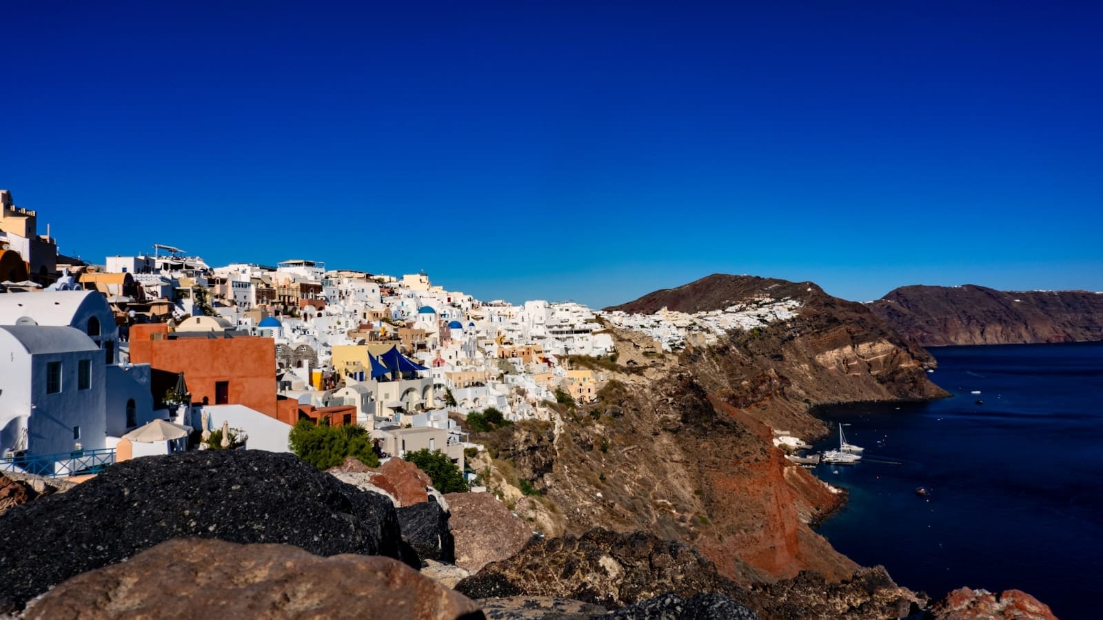Vista das vilas na falésia de Santorini com casas caiadas de branco, rocha vulcânica e mar azul profundo sob um céu intensamente azul, destacando as paisagens dramáticas e escondidas da ilha.