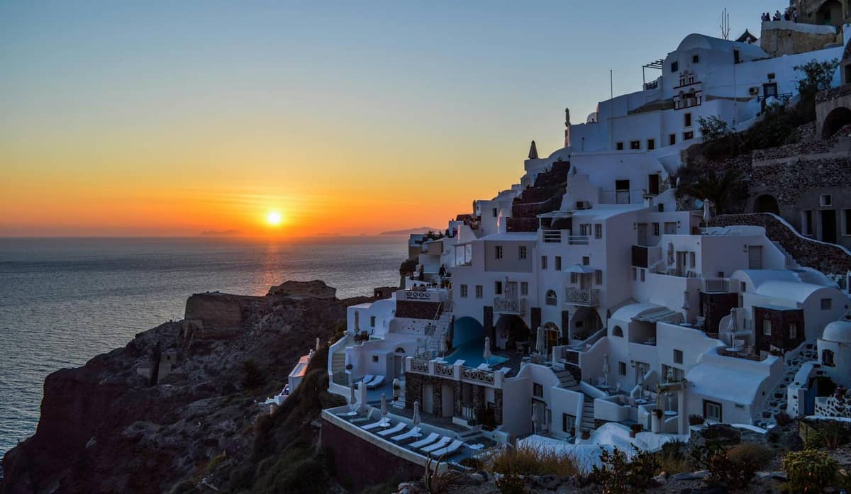 Edificios en los acantilados de Santorini con vistas al mar al atardecer, con el sol bajo en el horizonte, capturando una vista clásica del ocaso.