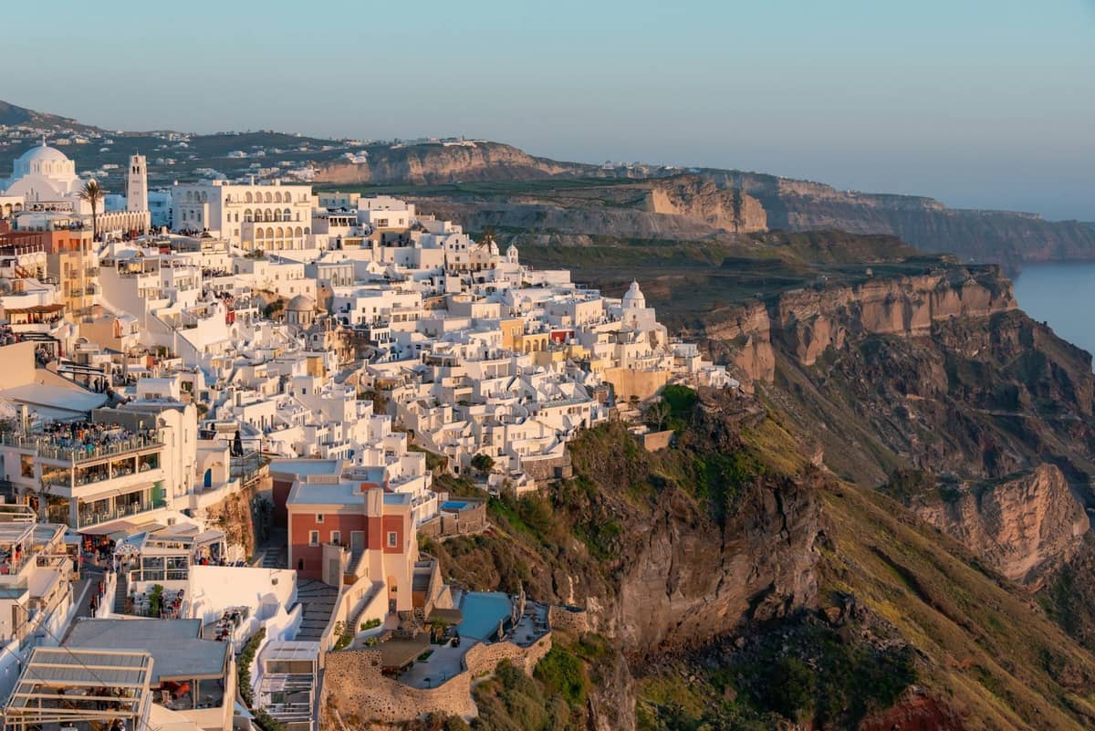 Edificios encalados de Santorini alineados en lo alto de los dramáticos acantilados de la caldera, con vistas al mar azul profundo bajo un cielo despejado.