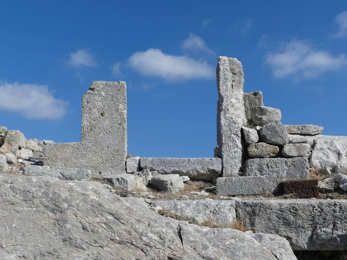 Alte Steinruinen mit aufrechten Mauern vor einem blauen Himmel, wahrscheinlich Teil einer archäologischen Stätte in Santorini.