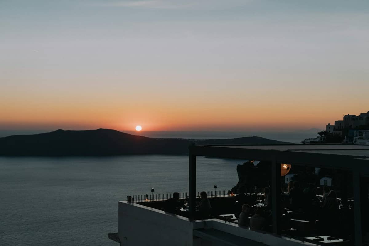 Sonnenuntergangsblick von einem Dachrestaurant mit Gästen, die den Santorini-Krater und das Meer überblicken.