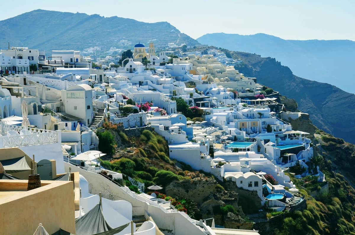 Weite Aussicht auf die ikonischen weiß getünchten Klippenhotels und Villen von Santorini mit Blick auf die Caldera, mit Pools und Terrassen, ideal für einen Flitterwochen-Aufenthalt.