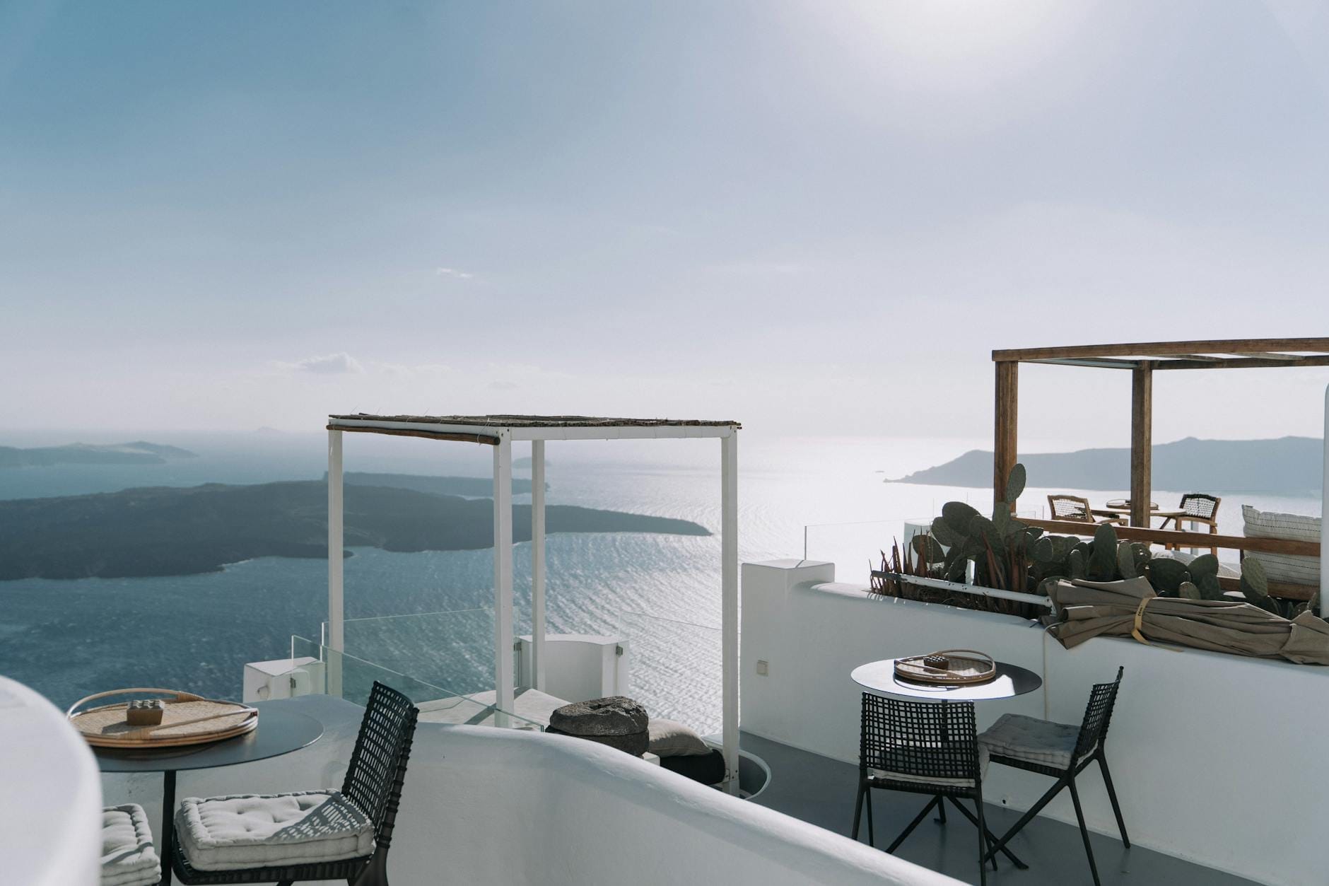 Terraço sofisticado na falésia com mobiliário elegante ao ar livre, com vista para o mar azul e a caldeira de Santorini ao pôr do sol — a essência do relaxamento de alto padrão.