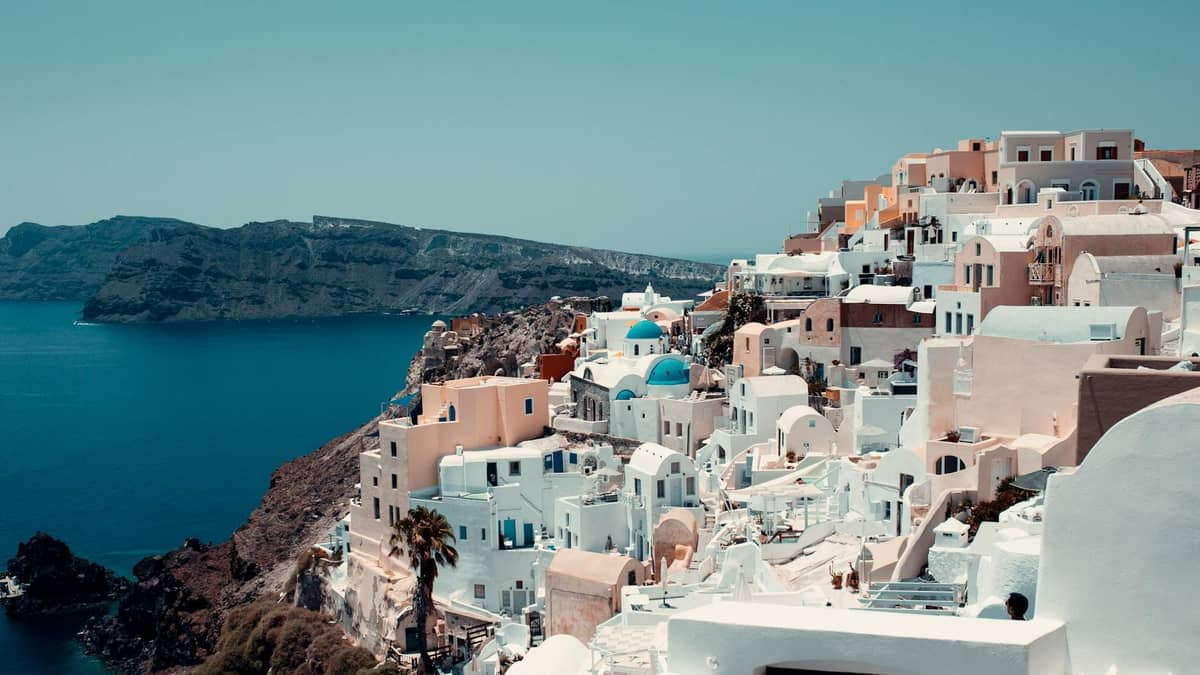 Vista diurna de las icónicas casas encaladas y las iglesias de cúpulas azules de Santorini encaramadas en los acantilados con vistas al brillante mar azul.