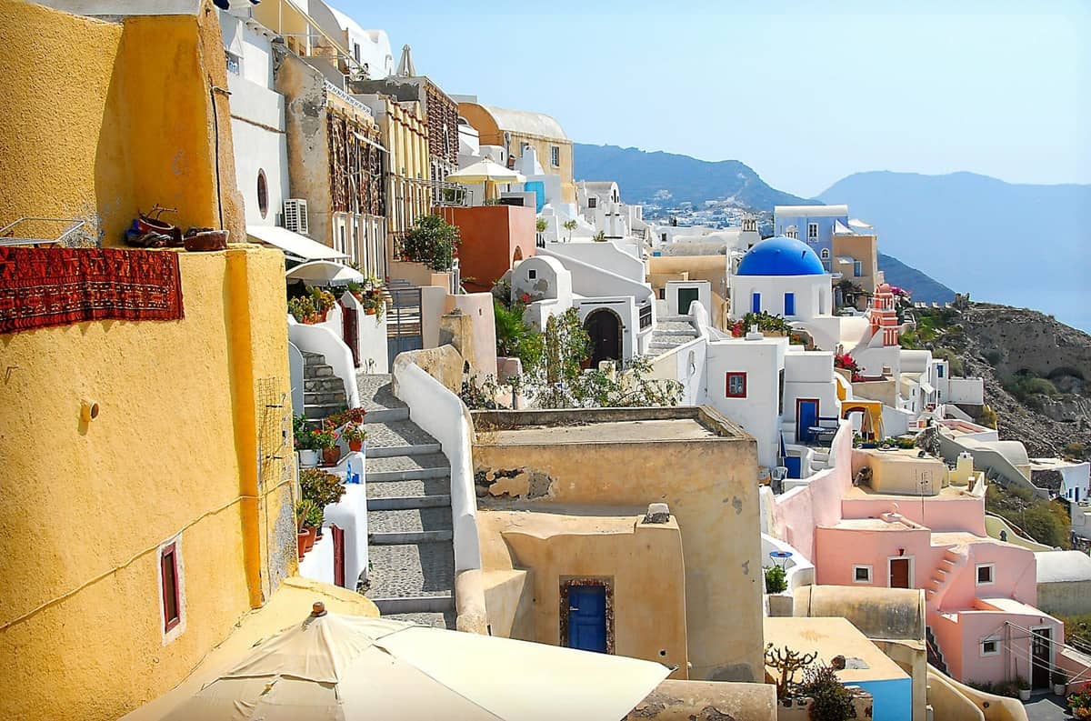 Escena del pueblo de Santorini con casas de colores, iglesias de cúpula azul, callejuelas estrechas y arquitectura cicládica tradicional bajo un cielo despejado.