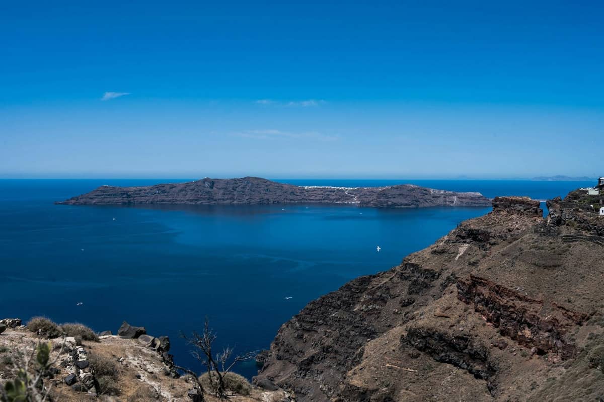Acantilados volcánicos y costa rocosa de Santorini con mar azul e isla de la caldera bajo cielo despejado