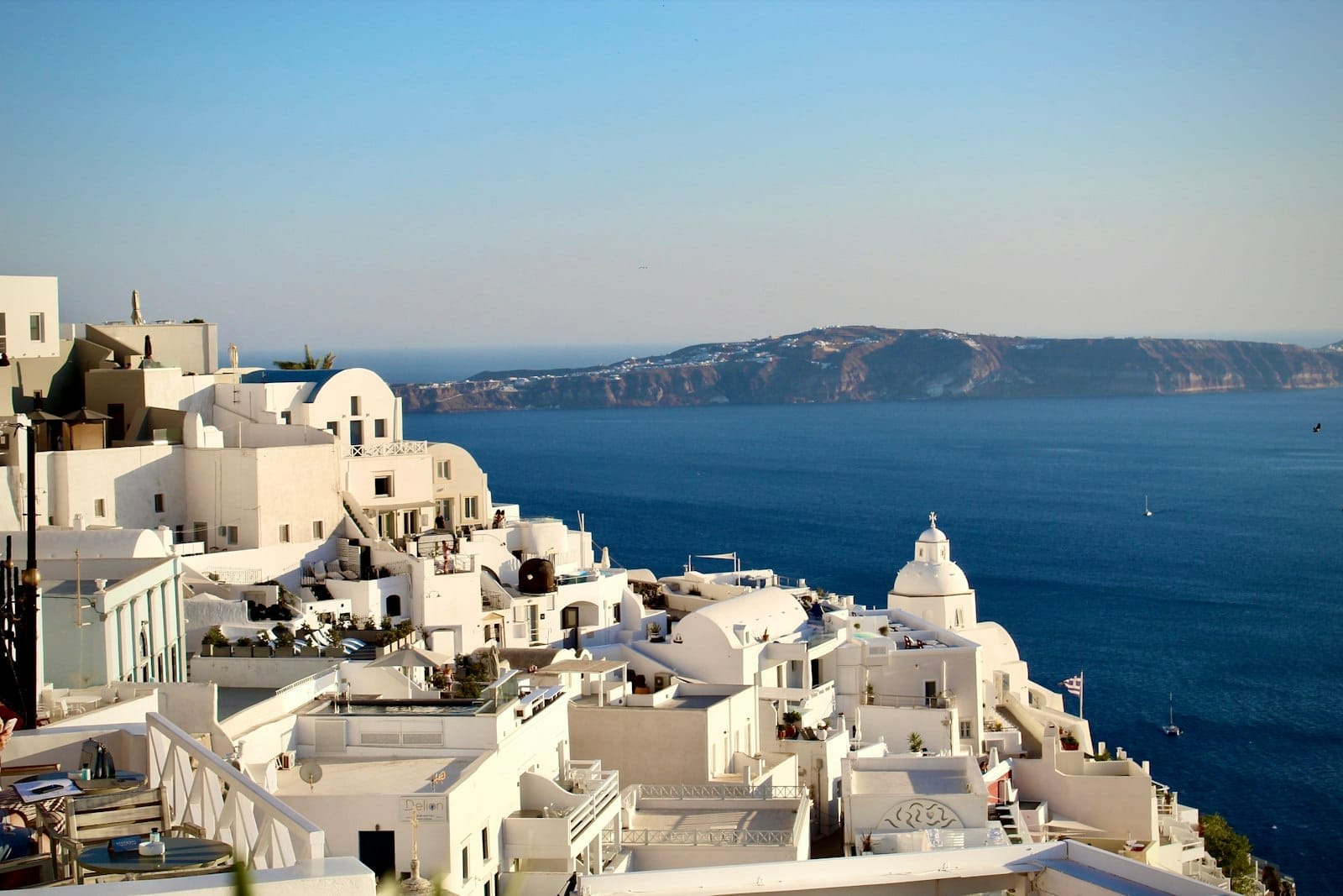Vista panorâmica dos icônicos prédios brancos de Santorini com cúpulas azuis sobre a caldeira e o profundo mar Egeu azul em um dia de céu limpo.