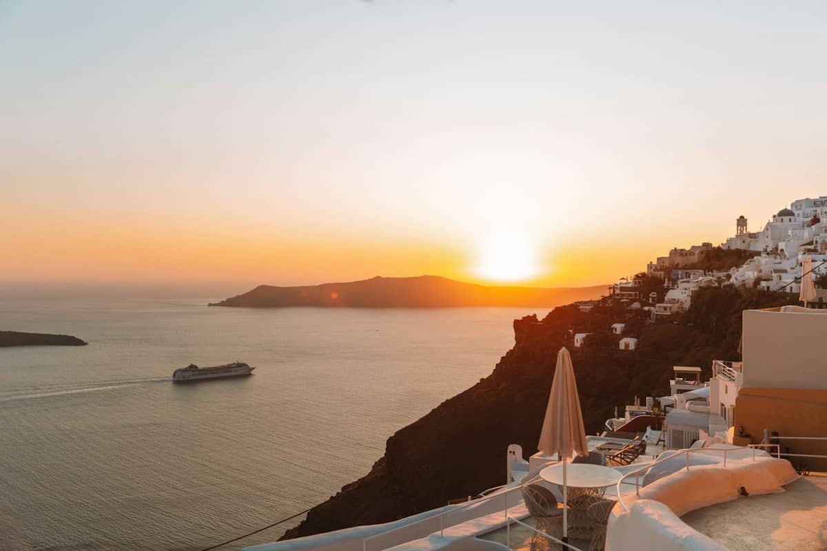 Atardecer dorado sobre Santorini con tranquilas terrazas encaladas y un crucero en la caldera, evocando una luz vespertina serena y excepcional.