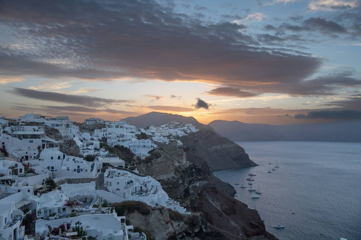 Vista ampia dal bordo della caldera a Santorini al tramonto, con edifici bianchi raggruppati su scogliere spettacolari sopra il mare.