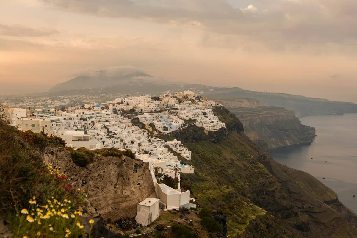 Gli iconici edifici bianchi di Santorini arroccati spettacolarmente sulle scogliere vulcaniche sopra la caldera blu profondo, con ampie viste sul mare sotto un cielo nebbioso.