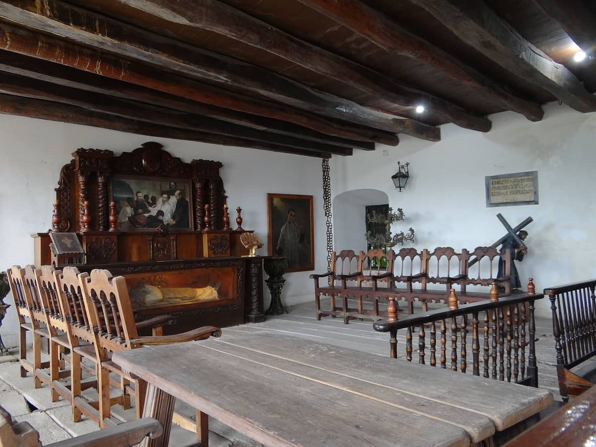 Wooden benches, religious paintings, and rustic beams decorate an interior room of Santuario de San Pedro Claver in Cartagena.